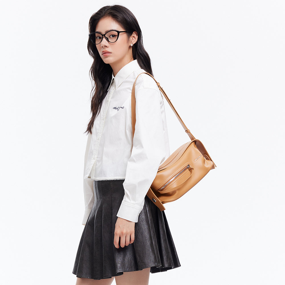 Woman in white Amazing Song shirt, black skirt, glasses, and tan shoulder bag on white background
