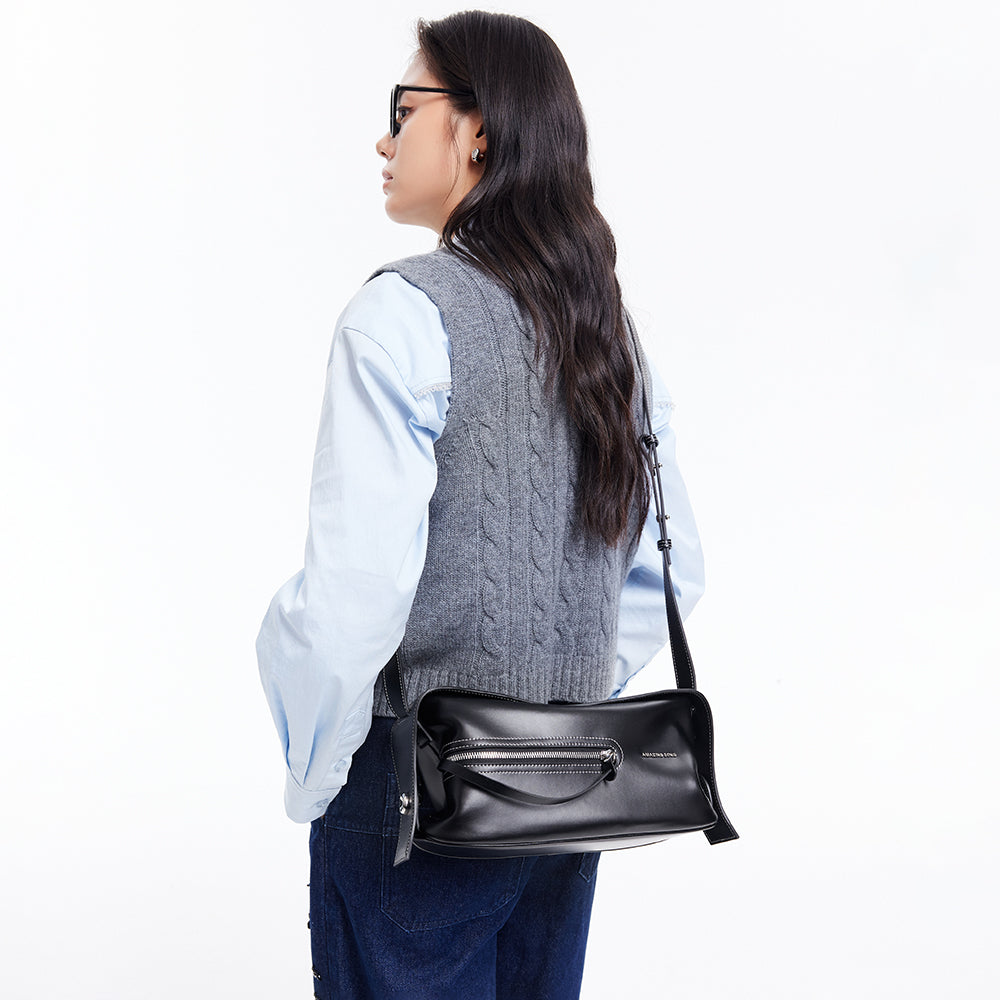 Woman wearing grey knit vest, light blue shirt, sunglasses, and black Amazing Song shoulder bag