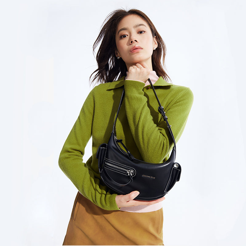 Woman in green sweater and brown skirt holding black Amazing Song shoulder bag