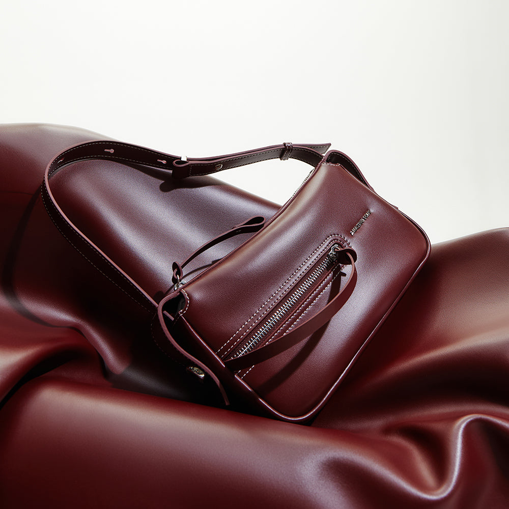 Burgundy leather shoulder bag with zipper detail on smooth burgundy surface, Amazing Song
