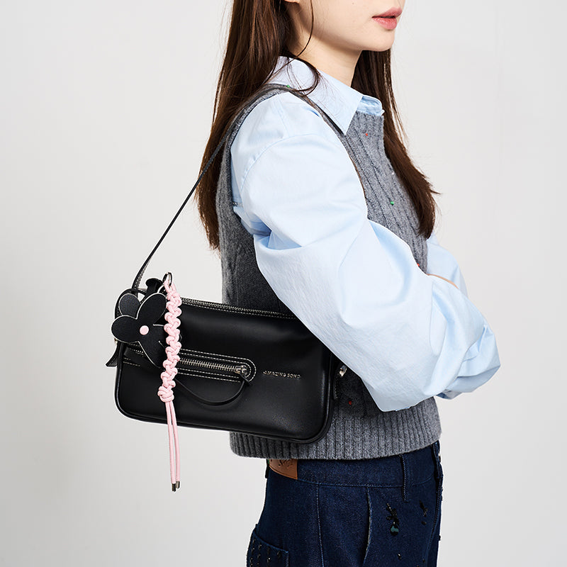 Woman wearing black shoulder bag with pink braided keychain, Amazing Song fashion accessory