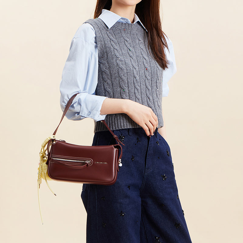 Woman holding maroon handbag, wearing grey sweater vest and blue shirt, Amazing Song fashion