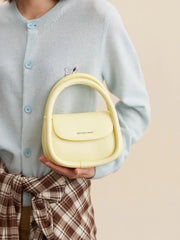 Woman holding yellow Amazing Song handbag, pastel sweater, plaid skirt, stylish accessories