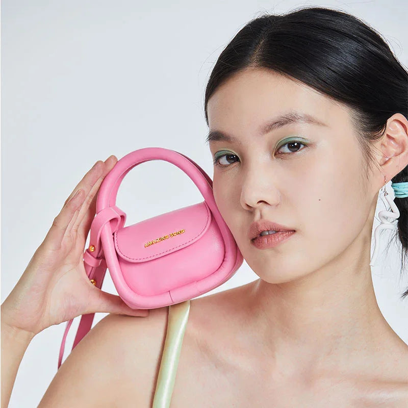 Woman holding pink Amazing Song mini handbag near face, stylish accessory close-up