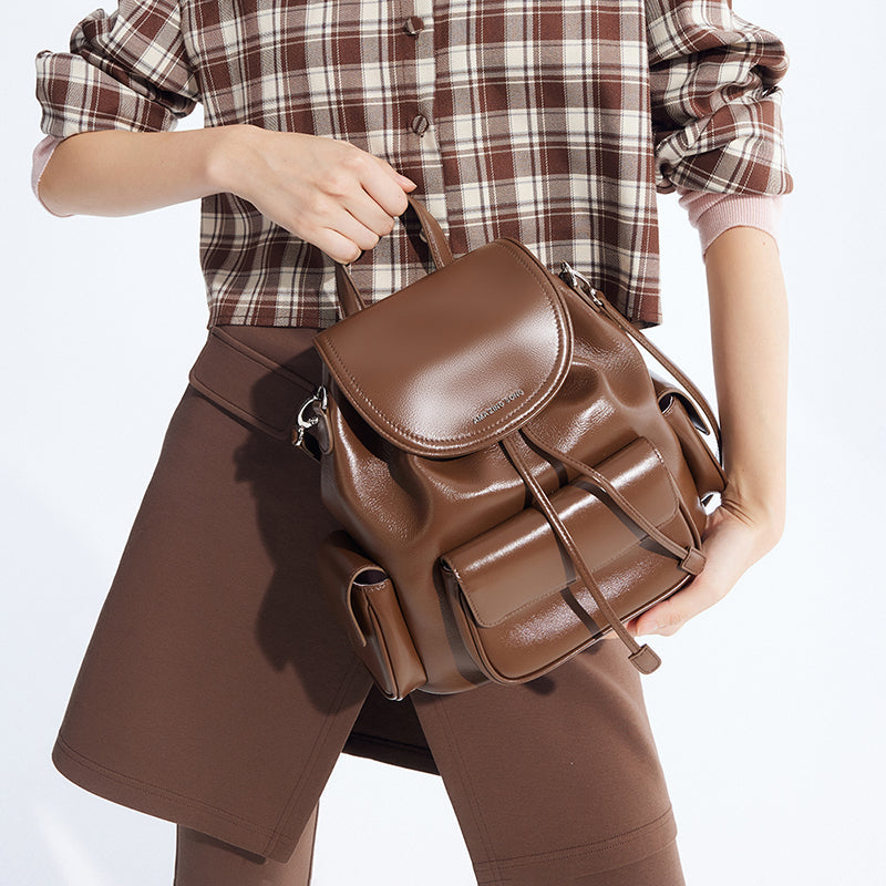 Woman holding brown leather backpack, plaid shirt and brown skirt, Amazing Song bag