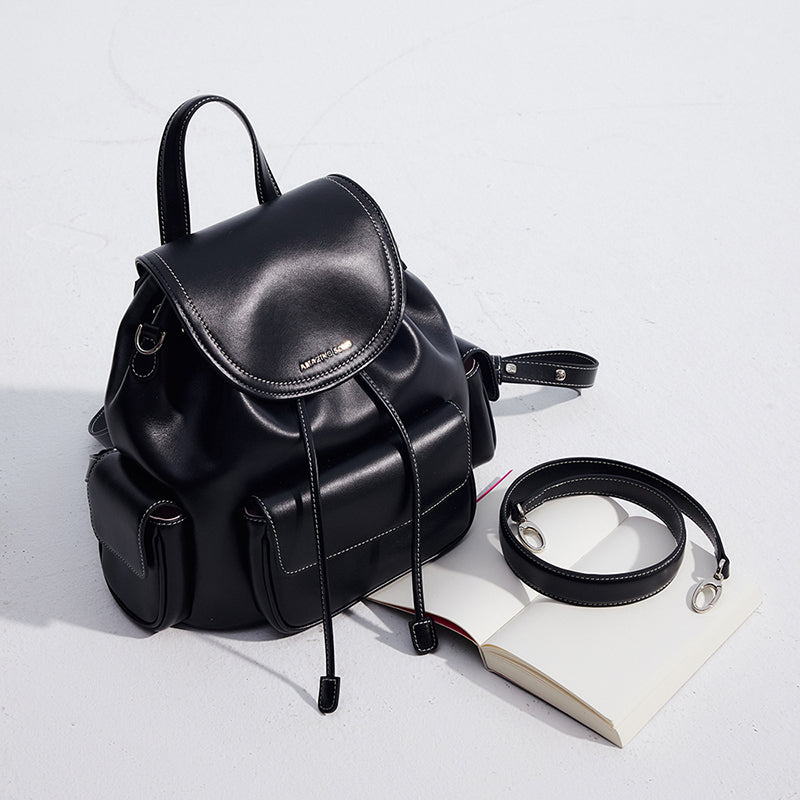 Sleek black leather backpack with side pockets beside an open book and detachable strap
