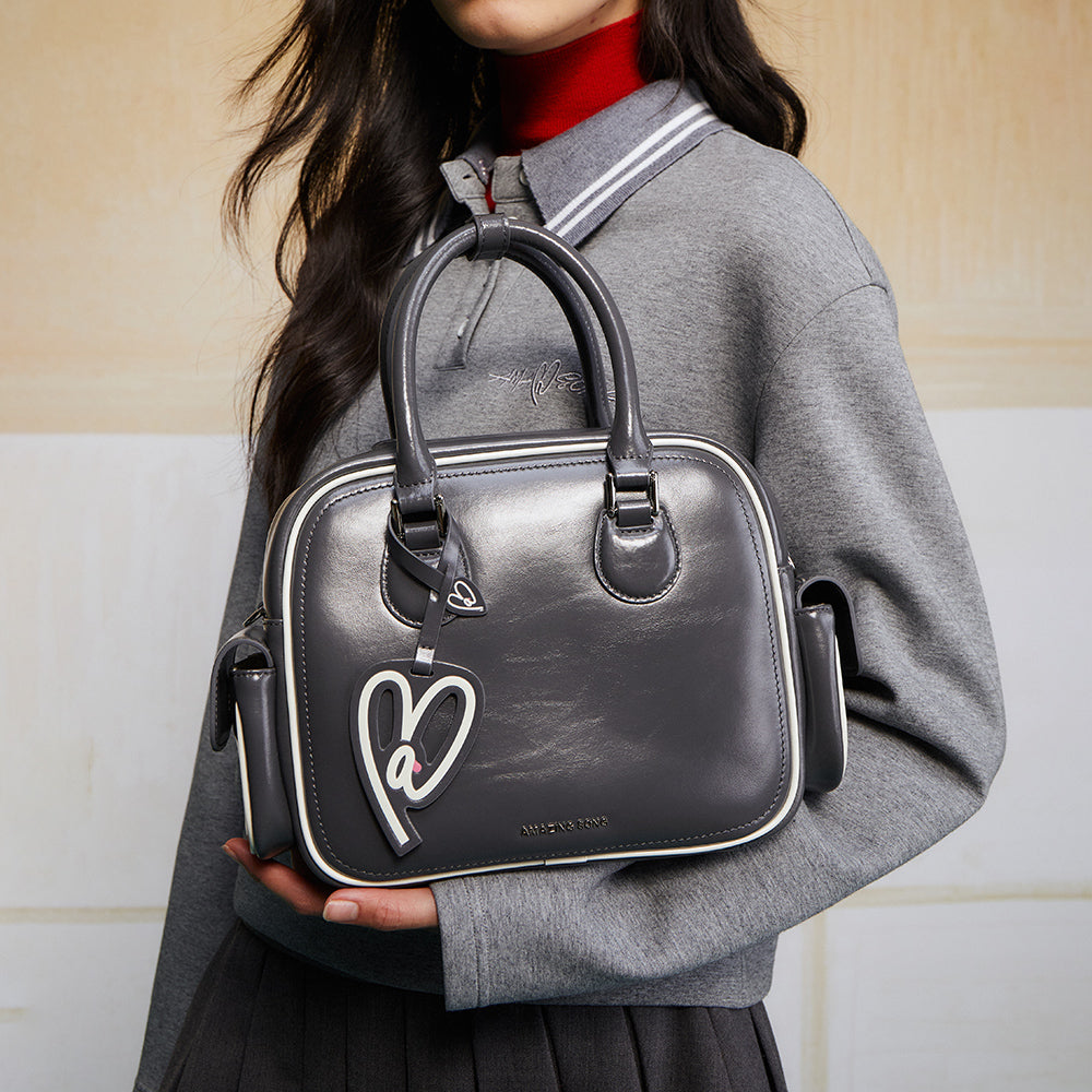 Woman in grey top holding a stylish black Amazing Song handbag with heart charm