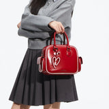 Woman in grey sweater and skirt holding glossy red handbag with heart charm, Amazing Song