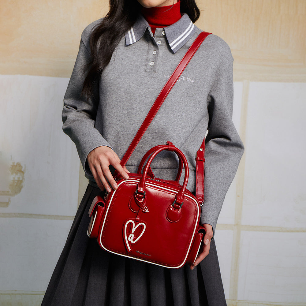 Woman in grey top with pleated skirt carrying a stylish red Amazing Song handbag.