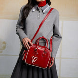 Woman in grey top with pleated skirt carrying a stylish red Amazing Song handbag.