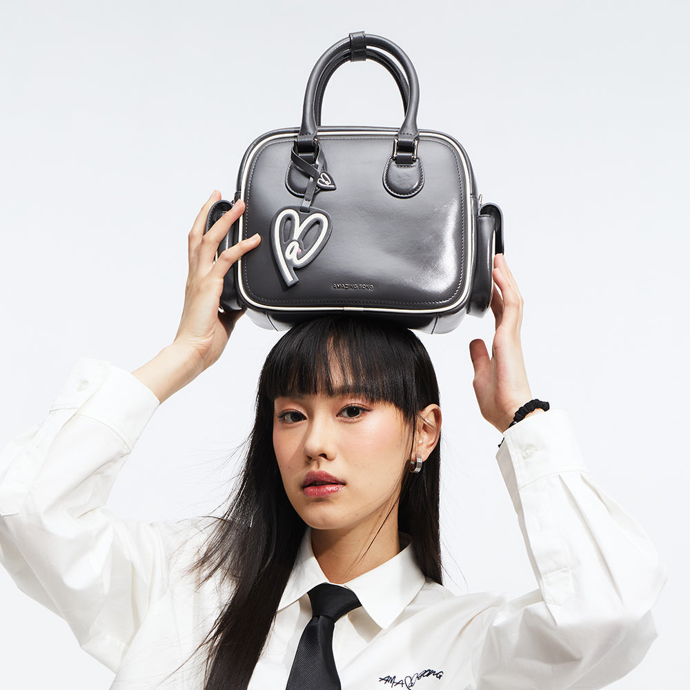 Woman in white shirt with black tie holding black Amazing Song handbag on her head