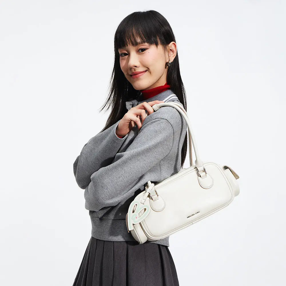 Woman with straight hair in gray outfit holding white Amazing Song handbag with rabbit charm