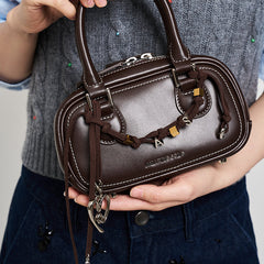 Brown leather Amazing Song handbag with gold accents and charm, held by person in grey sweater