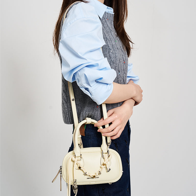 Woman wearing blue shirt and gray vest with cream Amazing Song shoulder bag