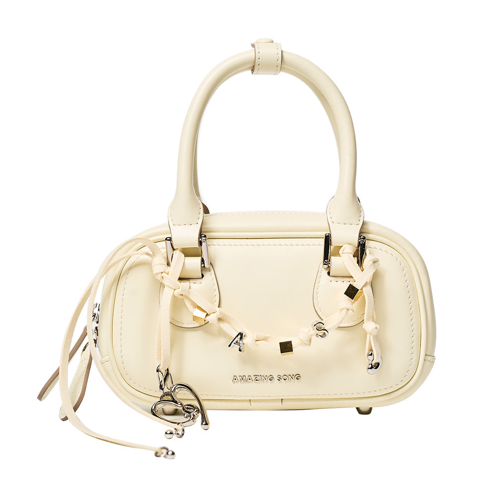 Cream Amazing Song handbag with decorative charms and dual handles on white background
