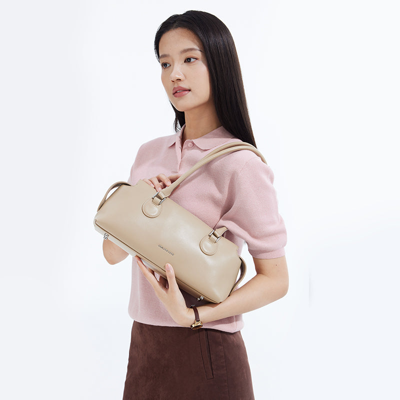 Woman in pink top holding beige Amazing Song handbag, minimalist background